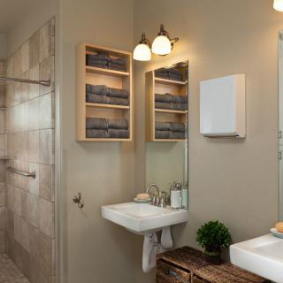 A modern bathroom with a wall-mounted sink, mirror, and built-in lighting. Shelves hold neatly folded towels, while a small plant adds a touch of greenery.