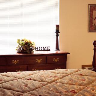 A cozy bedroom featuring a dresser adorned with a candle, flowers, and a 'HOME' sign.