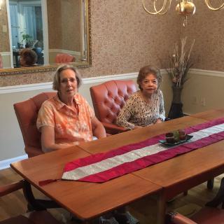 Two individuals seated at a dining table in a warmly decorated room.