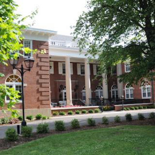 A classic brick building featuring elegant columns, surrounded by well-maintained greenery.