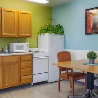 A cozy kitchen area with wooden cabinets, a refrigerator, stove, and microwave, complemented by a dining table with chairs and indoor plants.