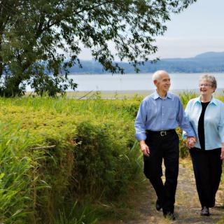 An elderly couple walking hand in hand along a scenic lakeside pathway.