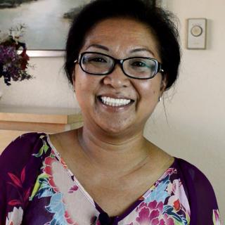 A woman wearing glasses and a floral shirt is smiling indoors.