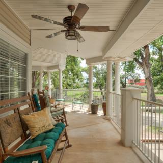 A cozy porch with rocking chairs, cushions, and a ceiling fan overlooking a lush outdoor area.