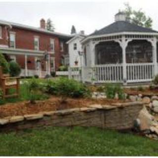 A picturesque garden with a white gazebo and a brick house in the background.