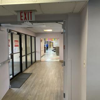 A hallway in a hospital or office building featuring an exit sign and glass doors.