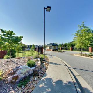 A quiet street with a gate, flanked by trees and landscaped areas under a clear blue sky.