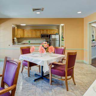 A cozy dining area with a table set for four, adorned with flowers, adjacent to a kitchen.
