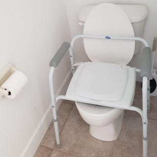 A bathroom equipped with a raised toilet seat and support frame for accessibility.