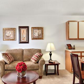 A cozy living room with a comfortable sofa, coffee table adorned with flowers, and dining area in the background.