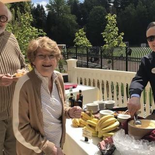 A group of people enjoying an outdoor gathering with a buffet table of food in a sunny setting.