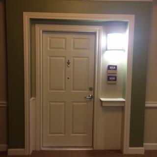A neatly framed apartment door with a light fixture and room numbers displayed.