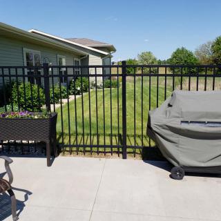 A backyard patio with a grill, fenced lawn, and outdoor seating.
