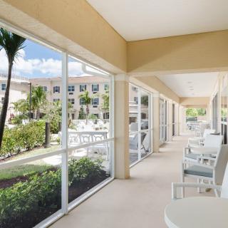 A spacious outdoor patio with white seating, offering a garden view through large windows.