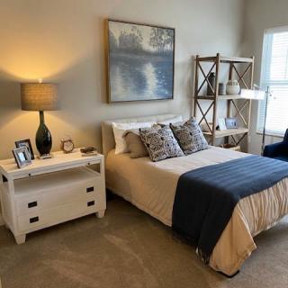A cozy bedroom with a neatly made bed, side table with a lamp, and decorative shelves.