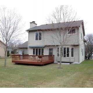 A view of a two-story residential house with a wooden deck in the backyard.