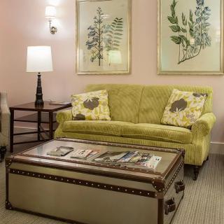 A cozy living room with a green sofa, a unique trunk-style coffee table, and botanical artwork on the wall.