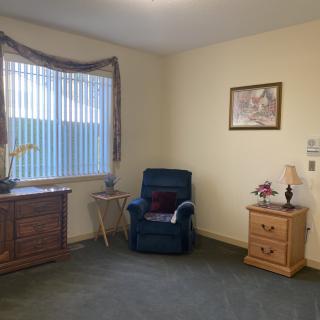A cozy living room with a blue chair, wooden furniture, and a large window.