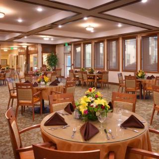 A well-decorated dining room with neatly arranged tables and chairs, featuring floral centerpieces and warm lighting.