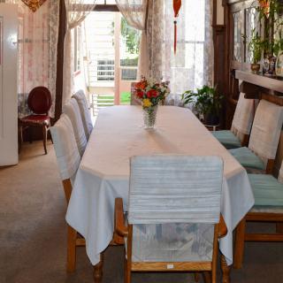 A cozy dining room with a table covered by a white tablecloth, surrounded by chairs and adorned with a vase of flowers.