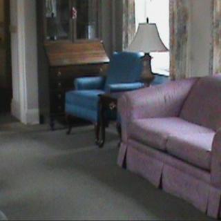 A cozy living room with a purple sofa, a blue armchair, and a lamp on a side table next to a wooden desk.