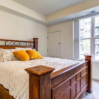 A cozy bedroom featuring a wooden bedframe with yellow accent pillows and a large window allowing natural light.