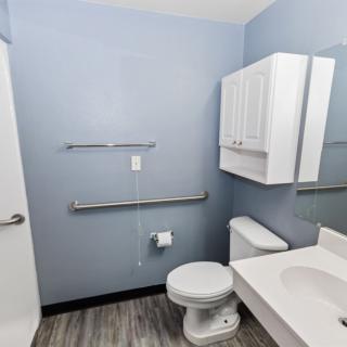 A modern bathroom with blue walls featuring a toilet, sink, cabinet, and towel rack.