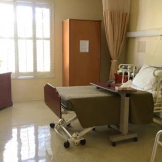 An empty hospital room with a single bed and a window letting in natural light.