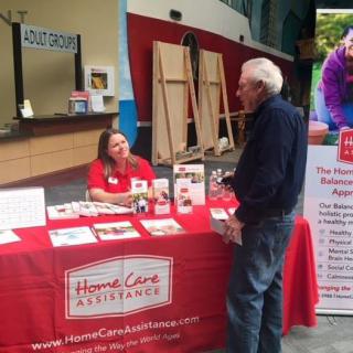 A representative at a healthcare assistance booth engaging with a visitor at an event.
