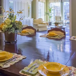 A bright dining room with a neatly set table, adorned with flowers and yellow dishware.