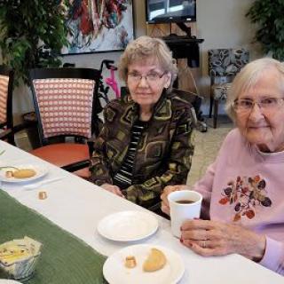 Two elderly women enjoying a meal and coffee at a community gathering.