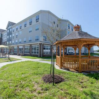 A modern multi-story building with a landscaped lawn and a wooden gazebo.