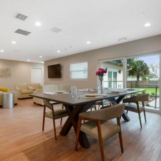 A modern dining room with a wooden table, chairs, and large sliding doors allowing natural light.