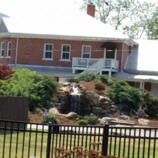 A brick house with a landscaped garden featuring a waterfall, surrounded by a fence.