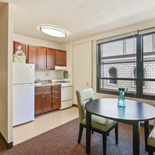 A cozy apartment kitchen and dining area with wooden cabinets, a table, and chairs.