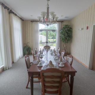 An elegantly set dining room table with a chandelier overhead and large windows draped with curtains.