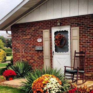 A cozy brick house with a rocking chair on the porch, adorned with autumn flowers and a festive wreath on the door.