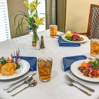 A neatly set dining table with two meals, iced tea, and a floral arrangement.