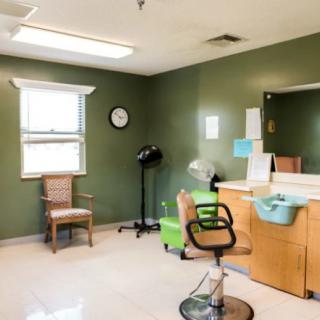 An empty hair salon room with green walls, featuring a styling chair, mirror, and salon equipment.