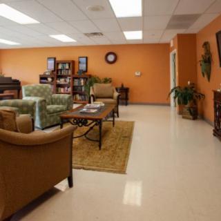 A cozy lounge area with comfortable seating, bookshelves, and indoor plants against an orange wall.