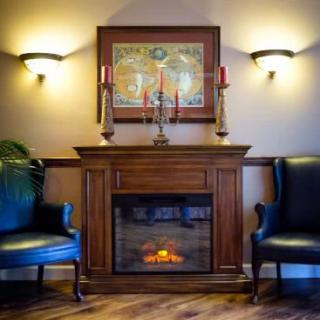 A cozy living room with a wooden fireplace flanked by two blue armchairs and adorned with artwork and candleholders.