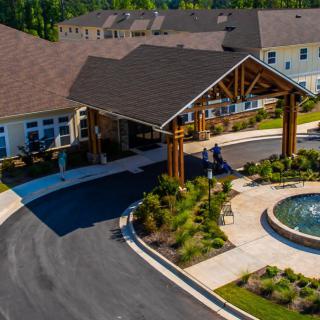 Aerial view of a residential building entrance with landscaped gardens and a circular driveway featuring a fountain.
