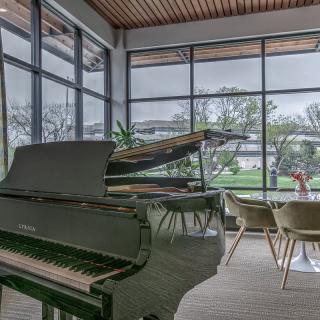 A modern lounge with a grand piano and large windows providing natural light.