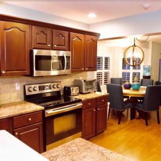 A modern kitchen with wood cabinets and stainless steel appliances, featuring an open layout adjacent to a dining area.