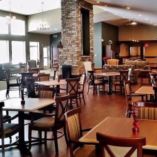 An empty restaurant dining area with tables, chairs, a brick wall, and natural lighting.