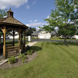 A quaint backyard with a wooden gazebo, well-maintained lawn, and clear blue sky.