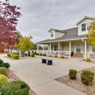 A charming house with a wide porch, surrounded by landscaped gardens and autumn trees, under a cloudy sky.