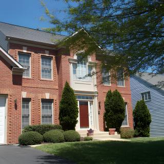 A suburban brick house with trees and bushes on a sunny day.