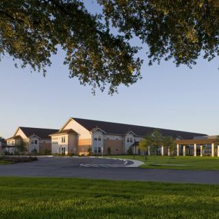 A scenic view of a large building surrounded by green grass and trees under a clear blue sky.