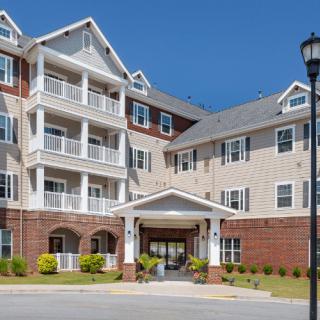 A modern apartment building with multiple balconies and a landscaped entrance under a clear blue sky.